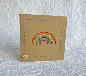 A hand stitched rainbow greetings card with wooden heart button detail. A blank, white paper insert is included for you to write your own message. Envelope included. Approximate size 10cmX 10cm. Made using 100% Cotton. Eco-friendly, Vegan friendly and fully recyclable. 