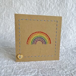 A hand stitched rainbow greetings card with wooden heart button detail. A blank, white paper insert is included for you to write your own message. Envelope included. Approximate size 10cmX 10cm. Made using 100% Cotton. Eco-friendly, Vegan friendly and fully recyclable.