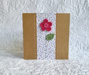 A single crocheted flower and leaf, with a hand stitched border. This small brown card has a blank white insert for your own message, and an envelope is included. Approximate size 10cm x 10 cm. Made using 100% cotton. Eco-friendly, Vegan friendly and fully recyclable.