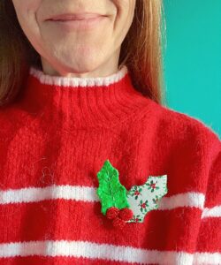 A handmade and hand stitched holly brooch. Made in green felt and holly patterned cotton fabric with red glass beaded berry details.
This brooch has a metal locking fastening on the back.
Approximate size 7cm height x 7.5cm wide.