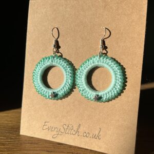 A handmade, crocheted pair of beaded hoop earrings, made using 100% cotton, glass beads and silver coloured metal stars and fixings. The earring hooks are made from a silver plated brass and are nickel, lead and cadmium free. Each earring measures approximately 3.4cm wide by 5cm Height (including hook). No plastic has been used. This item is Vegan and Eco-friendly, reusable and fully recyclable.