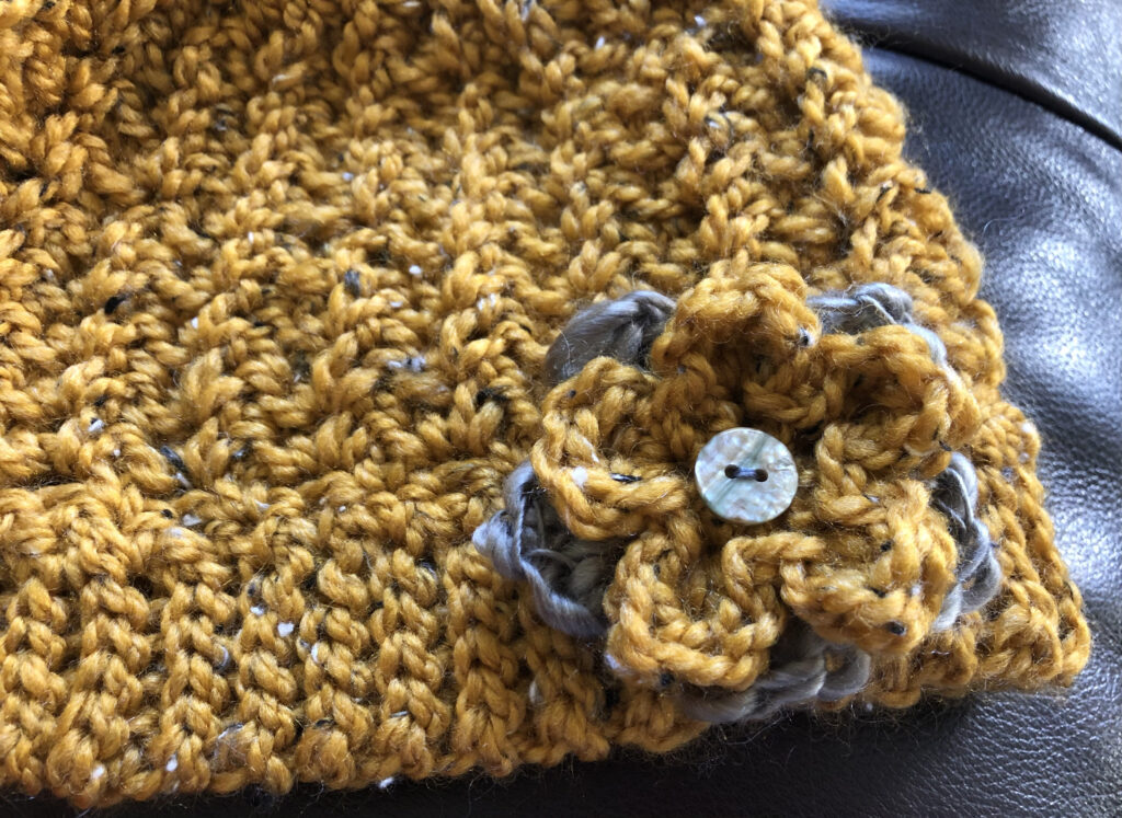 Chunky crocheted hat in a mustard colour with a double layered crocheted flower detail.