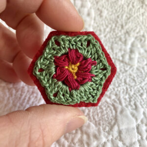 A hexagon shaped, hand stitched, felt and flower design crocheted brooch with locking brooch fixing.