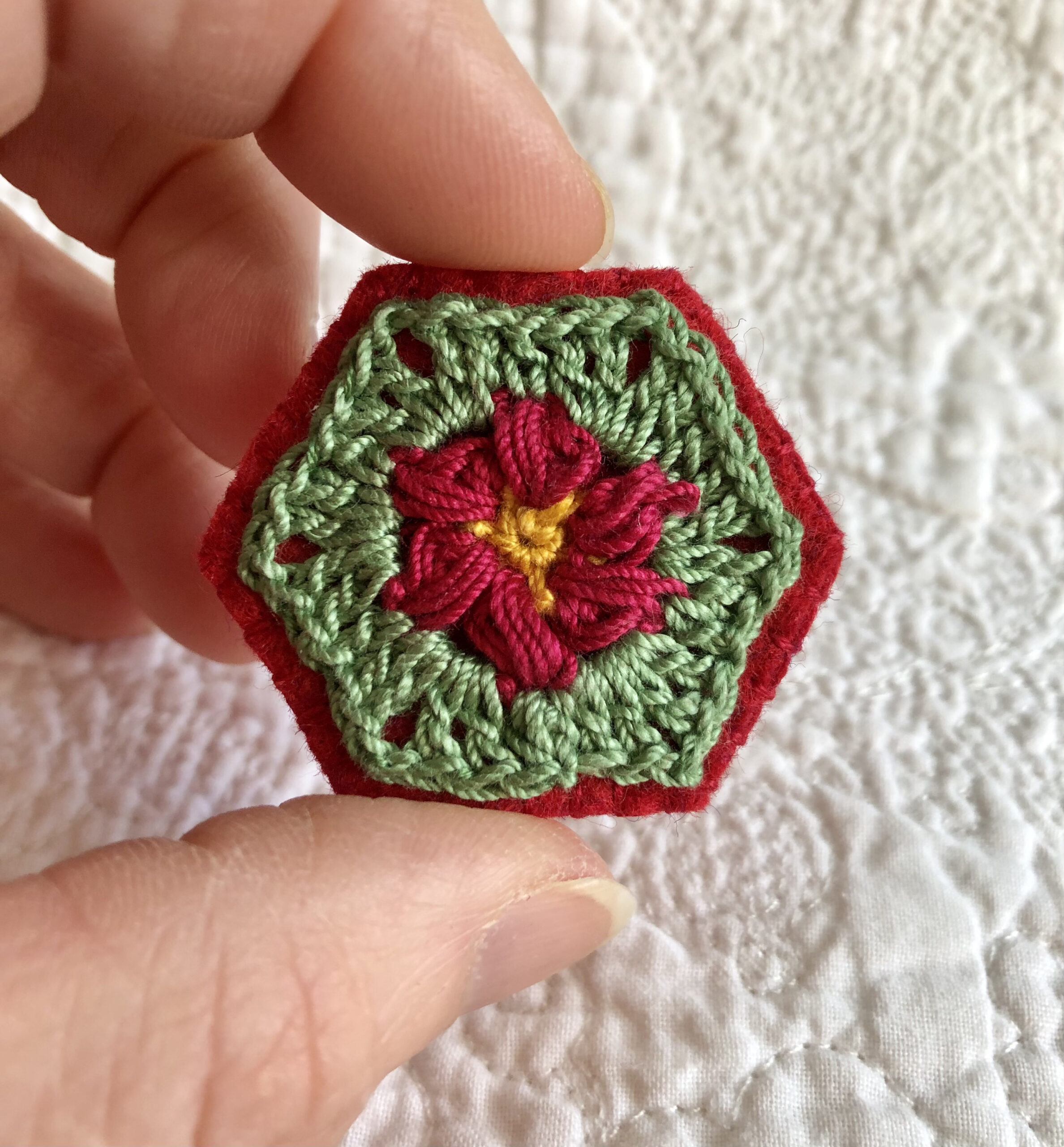 A hexagon shaped, hand stitched, felt and flower design crocheted brooch with locking brooch fixing.