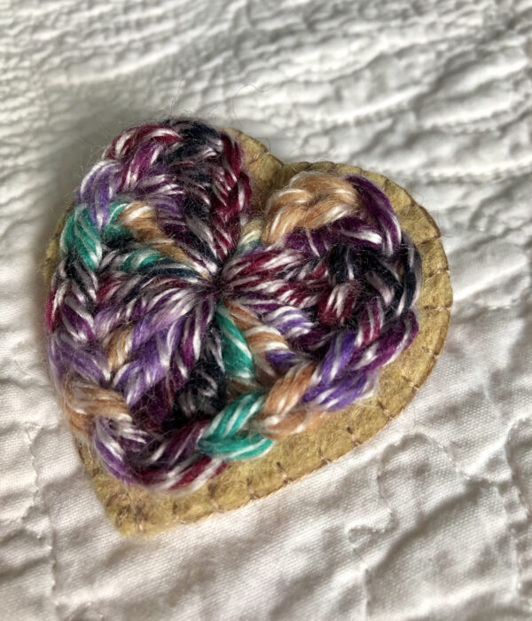 A crocheted heart on a hand stitched felt back with metal fixing brooch.