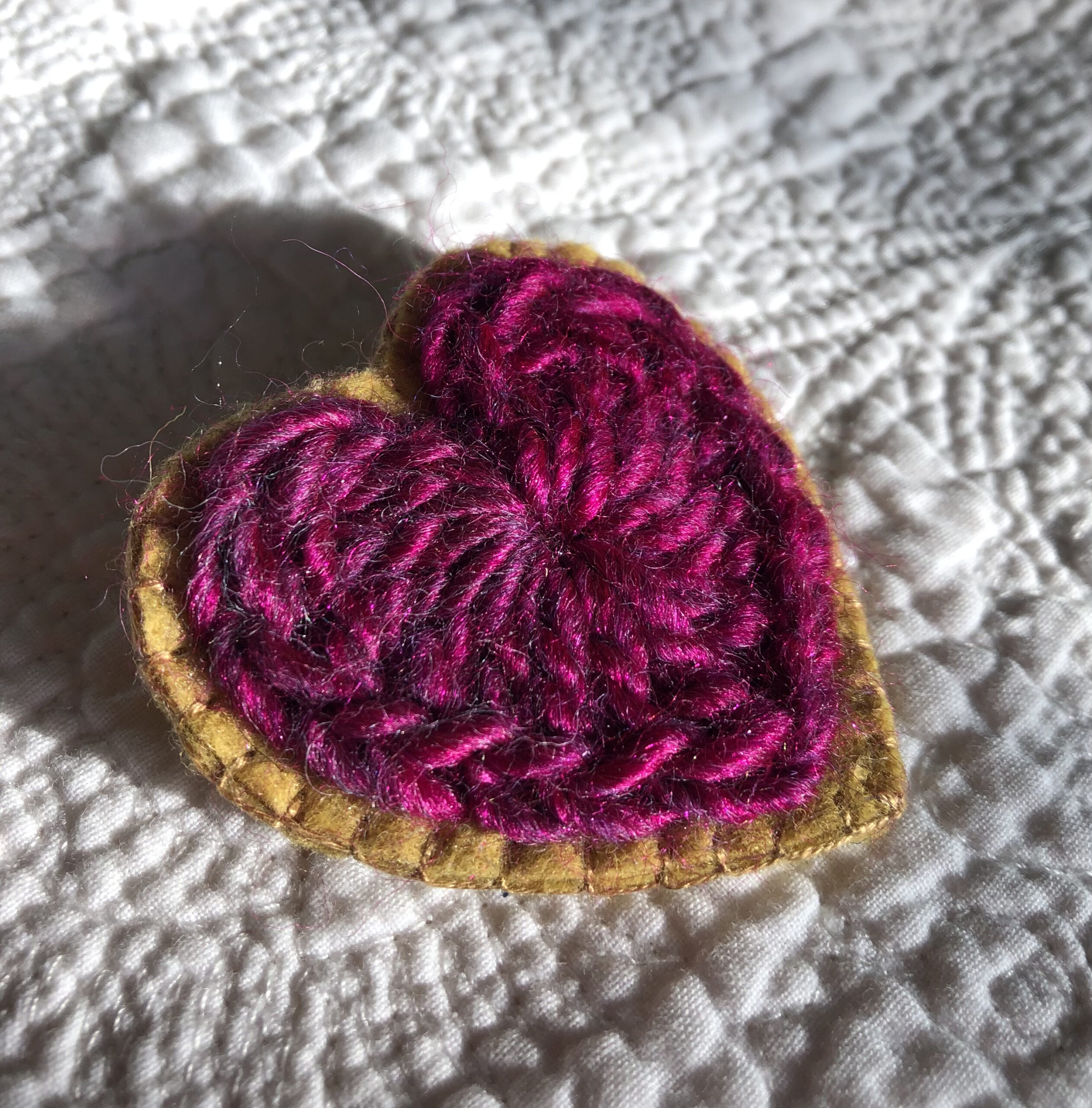 A crocheted heart on a hand stitched felt back with metal fixing brooch. Approximate size 6cm width x 6cm height.