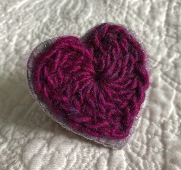 A crocheted heart on a hand stitched felt back with metal fixing brooch. Approximate size 6cm width x 6cm height.