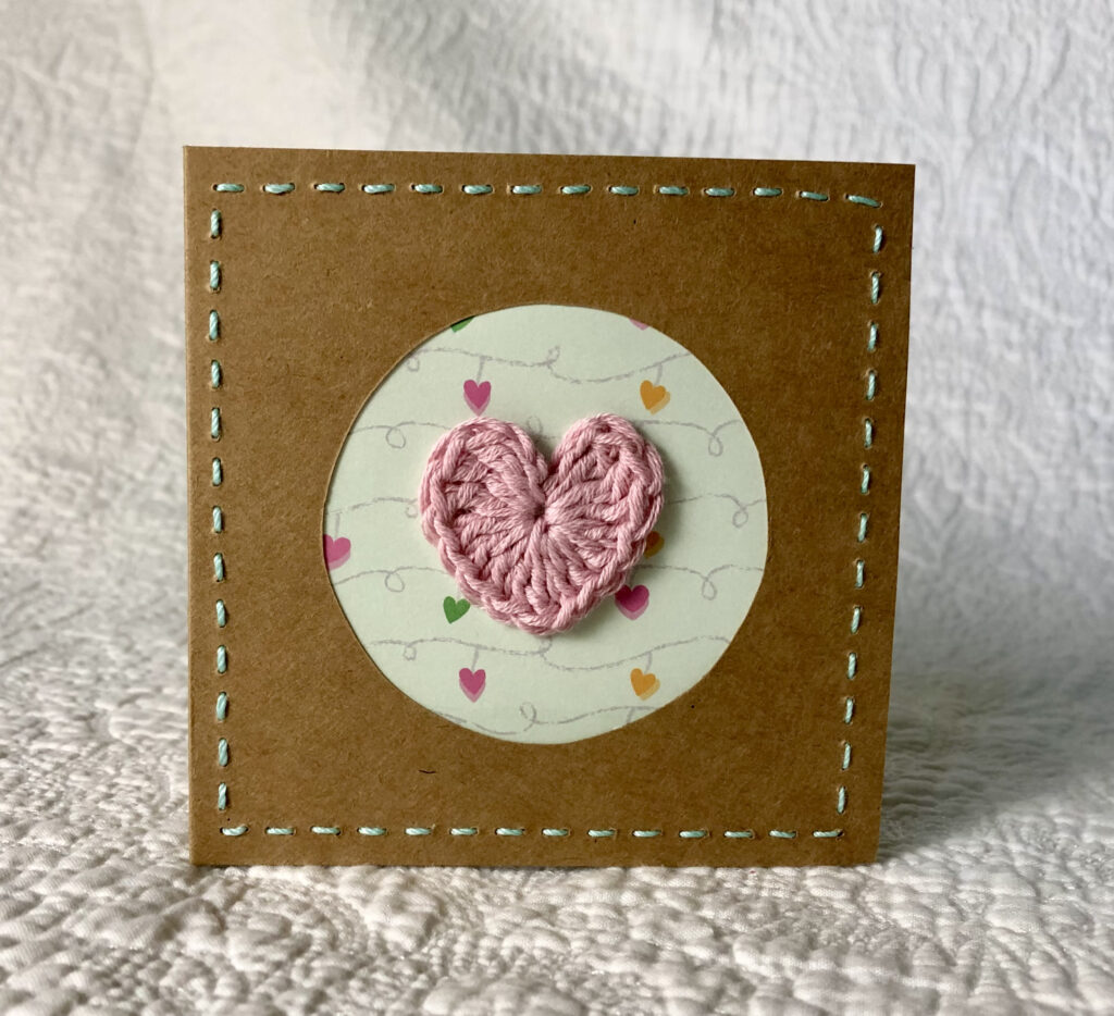 A single crocheted heart with hand stitched border on a small brown card (approximate size 10 x 10 cm)with blank white insert. Brown envelope included.
