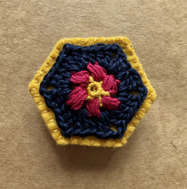 A hexagon shaped, hand stitched, felt and flower design crocheted brooch with locking brooch fixing.