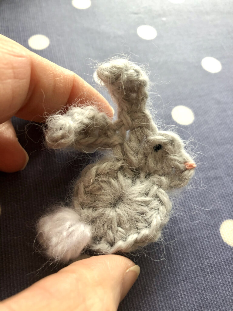 A handmade, crocheted grey bunny with white tail brooch.