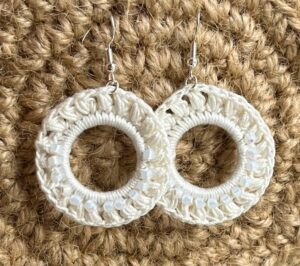 A handmade, crocheted pair of ivory coloured, half beaded hoop earrings, made using 100% cotton and glass beads with metal fixings. The earring hooks are made from a silver plated brass and are nickel, lead and cadmium free. Each earring measures approximately 3.4cm wide by 5cm Height (including hook). No plastic has been used. This item is Vegan and Eco-friendly, reusable and fully recyclable. 