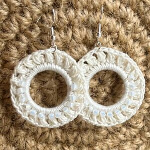 A handmade, crocheted pair of ivory coloured, half beaded hoop earrings, made using 100% cotton and glass beads with metal fixings. The earring hooks are made from a silver plated brass and are nickel, lead and cadmium free. Each earring measures approximately 3.4cm wide by 5cm Height (including hook). No plastic has been used. This item is Vegan and Eco-friendly, reusable and fully recyclable.