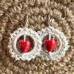 A handmade, crocheted pair of ivory coloured and red heart beaded hoop earrings, made using 100% cotton and ceramic heart beads with metal fixings. The earring hooks are made from a silver plated brass and are nickel, lead and cadmium free. Each earring measures approximately 3.4cm wide by 5cm Height (including hook). No plastic has been used. This item is Vegan and Eco-friendly, reusable and fully recyclable.
