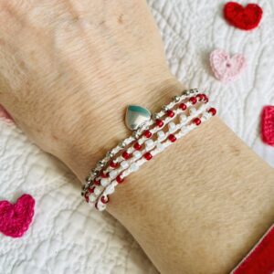 A handmade, crocheted and glass beaded bracelet with silver coloured metal heart charm. Fully adjustable with sliding metal bead fastening. 4 strands, made using 100% cream cotton and glass beads in 3 colours of dark red, pearlescent cream and silver. No plastic! Eco-friendly, vegan friendly and completely recyclable.