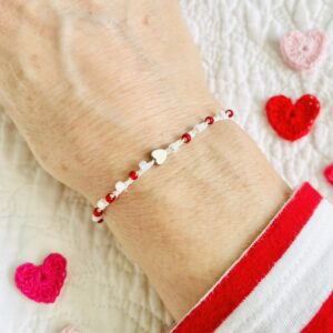 A handmade, single stranded beaded bracelet with a silver coloured metal heart, red and pearlescent cream glass beads. Made using 100% cotton and glass and metal beads/fixings. This item is fully adjustable. No plastic has been used. This item is Vegan and Eco-friendly, reusable and fully recyclable.