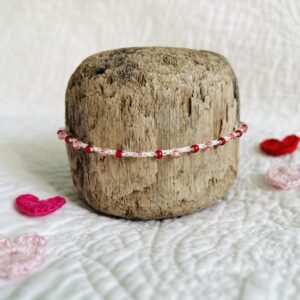 A handmade, crocheted, single stranded bracelet. Made using red and pink glass beads and 100% cream cotton with a fully adjustable sliding bead fastening. No plastic has been used. This item is Vegan and Eco-friendly, reusable and fully recyclable.