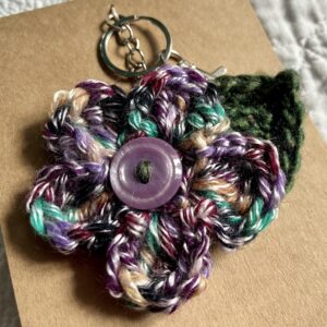 A hand crocheted multi-coloured flower and leaf with button detail keyring/bag charm.