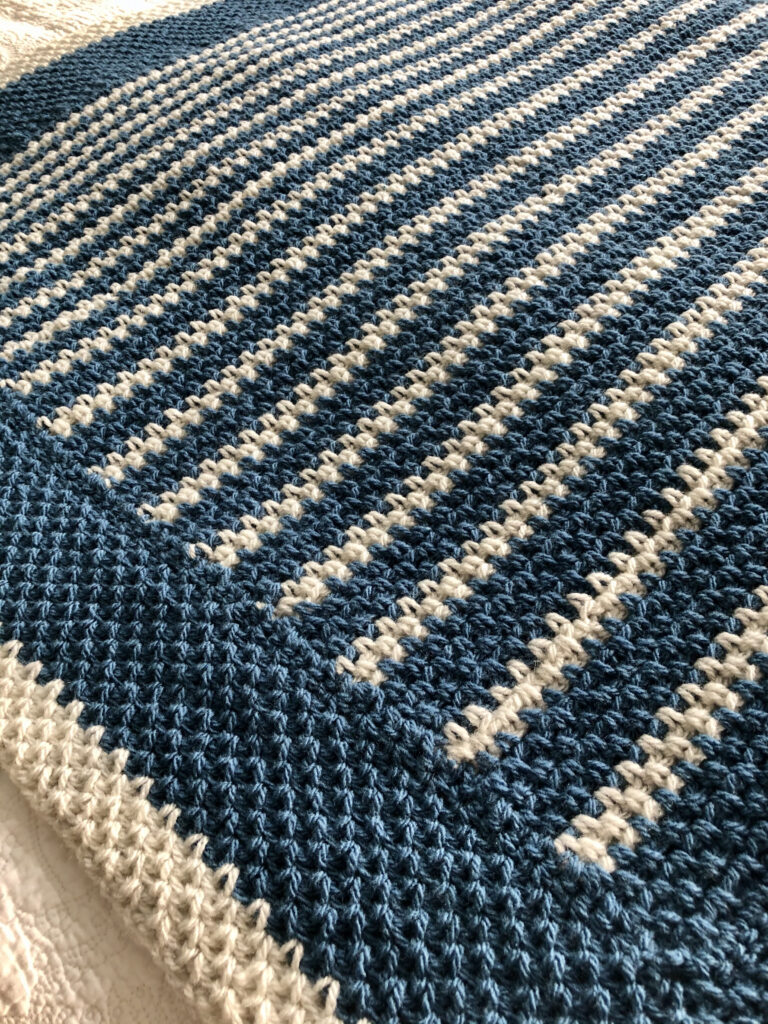 A handmade, crocheted blanket in Denim Blue and light cream. Made with 80%Acrylic/20% Wool mix yarn. 