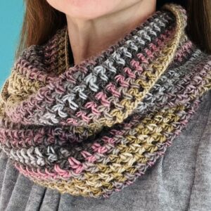 A loose fitting, double length infinity scarf made using a soft and lightweight yarn in a mix of subtle soft shades of pink, grey, green.