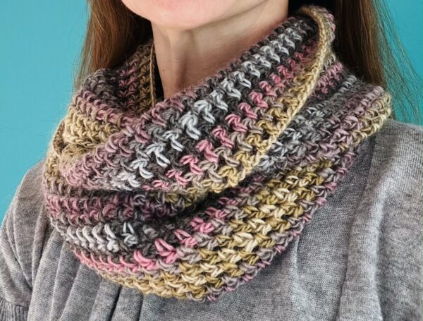 A loose fitting, double length infinity scarf made using a soft and lightweight yarn in a mix of subtle soft shades of pink, grey, green.