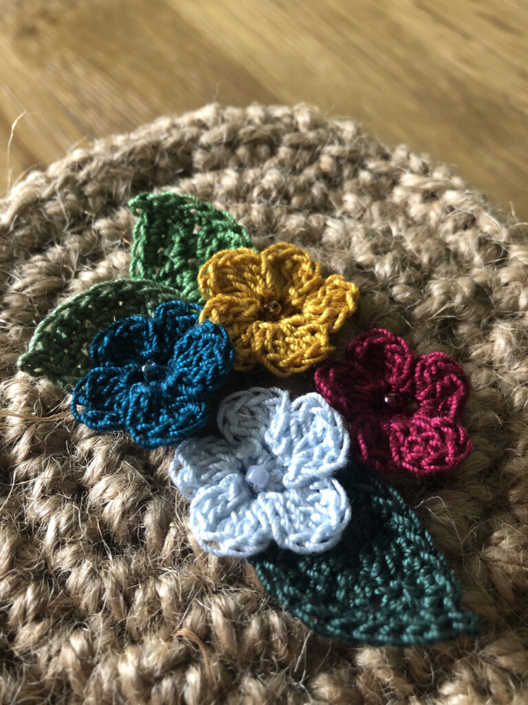 A handmade, crocheted 100% jute basket with lid. Decorated with 100% cotton crocheted flowers and leaves. Approximate size 7.5cm Height x 11.5cm width.