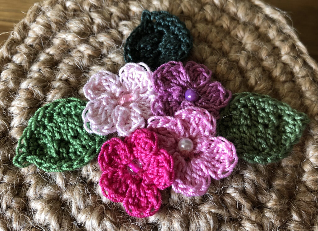 A handmade, crocheted 100% jute basket with lid. Decorated with 100% cotton crocheted flowers and leaves. Approximate size 7.5cm Height x 11.5cm width.