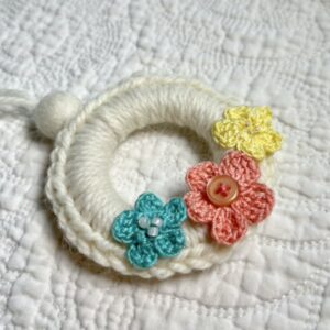 A mini crocheted and embellished Spring/Easter inspired flower wreath. Handmade using a wooden ring with a mix of acrylic, cotton and wool materials, glass beads and recycled buttons.