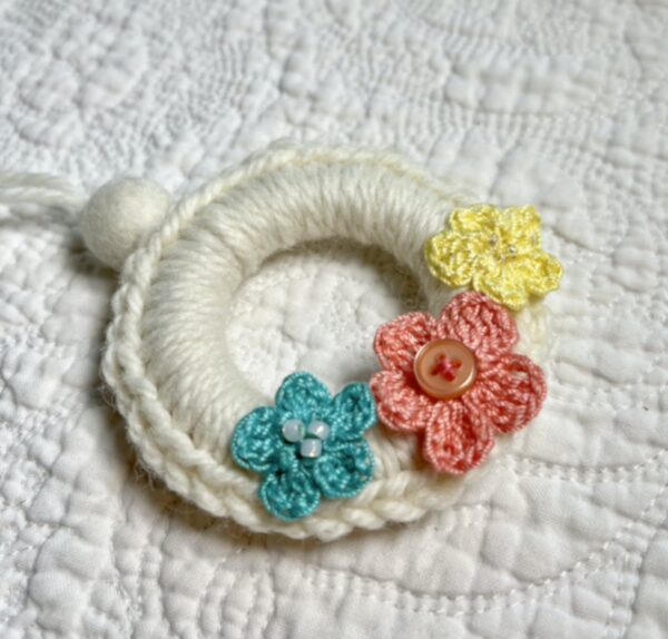 A mini crocheted and embellished Spring/Easter inspired flower wreath. Handmade using a wooden ring with a mix of acrylic, cotton and wool materials, glass beads and recycled buttons.