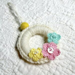 A mini crocheted and embellished Spring/Easter inspired flower wreath. Handmade using a wooden ring with a mix of acrylic, cotton and wool materials, glass beads and recycled buttons.