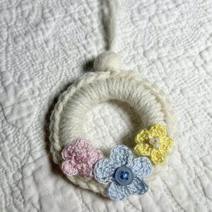 A mini crocheted and embellished Spring/Easter inspired flower wreath. Handmade using a wooden ring with a mix of acrylic, cotton and wool materials, glass beads and recycled buttons.