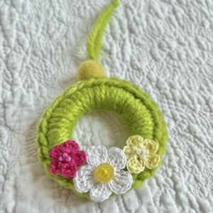 A mini crocheted and embellished Spring/Easter inspired flower wreath. Handmade using a wooden ring with a mix of acrylic, cotton and wool materials, glass beads and recycled buttons.