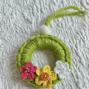 A mini crocheted and embellished Spring/Easter inspired flower wreath. Handmade using a wooden ring with a mix of acrylic, cotton and wool materials, glass beads and recycled buttons.