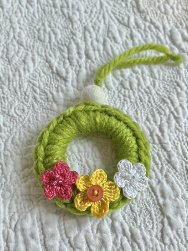 A mini crocheted and embellished Spring/Easter inspired flower wreath. Handmade using a wooden ring with a mix of acrylic, cotton and wool materials, glass beads and recycled buttons.
