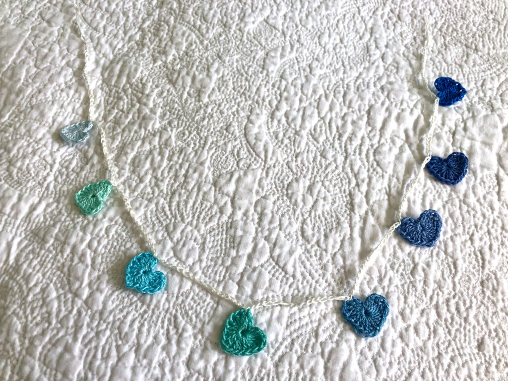 8 tiny crocheted hearts on a garland, in blues and greens. Made in 100% cotton.
