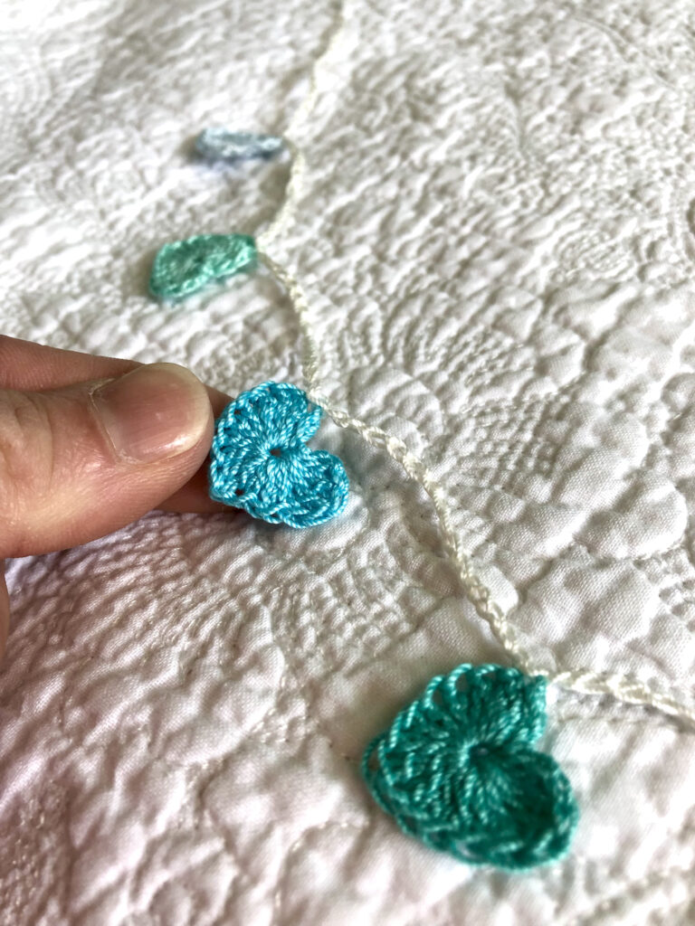 8 tiny crocheted hearts on a garland, in blues and greens. Made in 100% cotton.