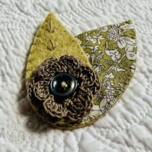 A single, double layered, crocheted flower in a coffee colour, with vintage button detail and two leaf brooch. Flower made using 100% Cotton with hand stitched felt and patterned fabric leaves. A locking metal brooch fastening on the back. Approximate size 7.5cm width x 6.5cm height.