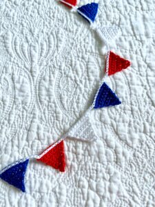 A garland of mini bunting triangles in Red, White and Blue on a white handing cord. Made using 100% Cotton. Eco and Vegan friendly. Reusable and fully recyclable. Approximate total length 90cm (but can stretch slightly). Each triangle measures approximately 3cm wide x 2.5cm height.