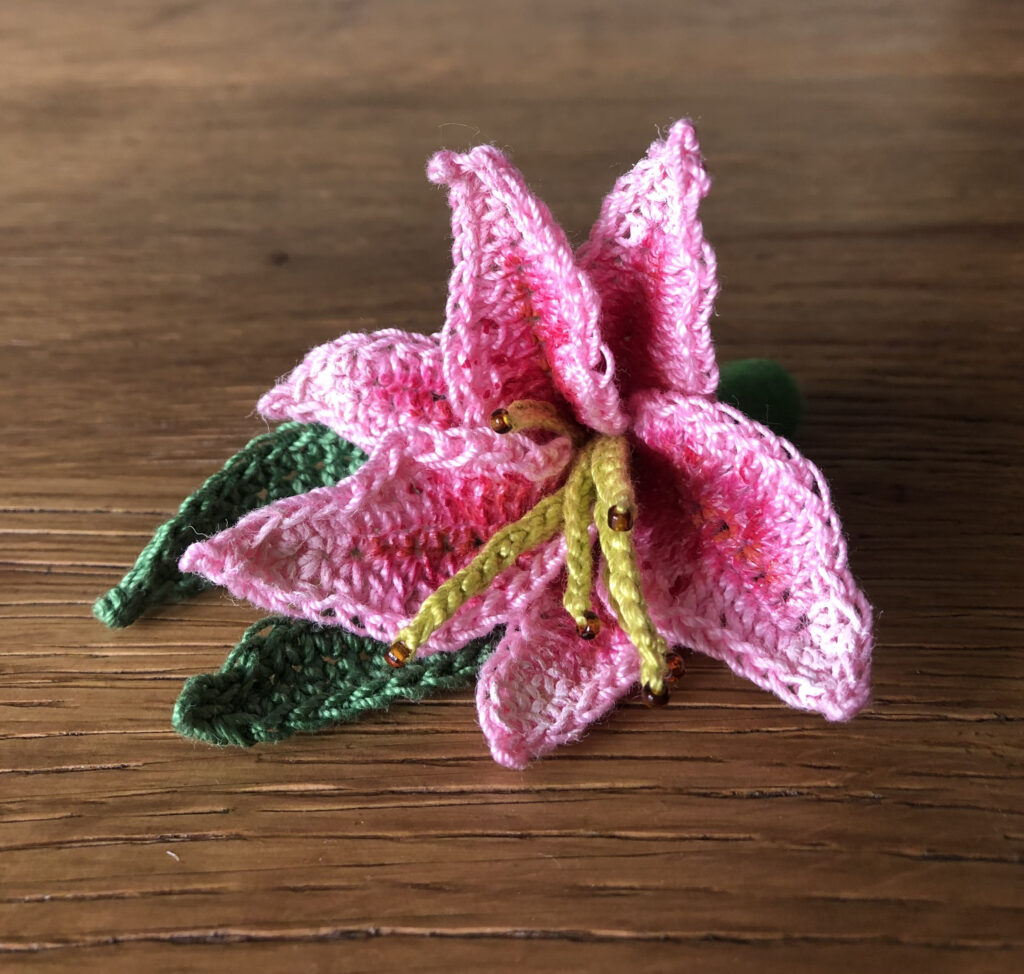 A hand crocheted and hand painted Lily flower and leaf brooch. Made using 100% cotton and glass beads.