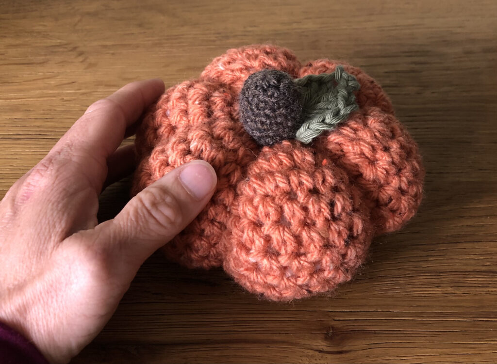 Chunky orange coloured, crocheted pumpkin with brown stalk and green leaf details.
