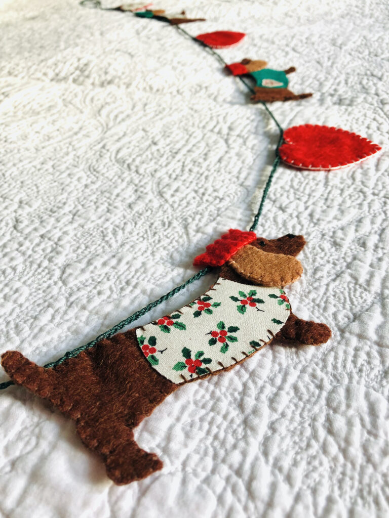 A garland of four Christmas dachshund dogs and 5 hearts. Hand cut and hand sewn, using a selection of felt and holly print cotton fabric. In a collection of red, green, brown and cream colours. Approximate total length 140cm.