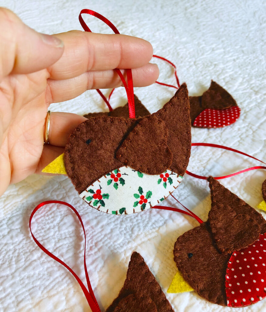 A hand cut and hand stitched, felt and fabric robin, with a red ribbon hanging loop. Robins approximate size 8cm w x 5cm h. (excluding hanging ribbon.)