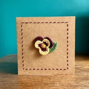 A single crocheted Burgundy and Yellow Pansy flower and a green leaf, with hand sewn boarder. This card has a blank white paper insert for you to write your own message. Handmade, using 100% cotton.