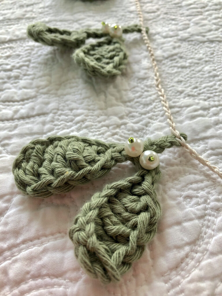 A handmade and  crocheted garland of 9 green mistletoe and pearl berry sprigs. Made using 100% cotton and glass beads. 